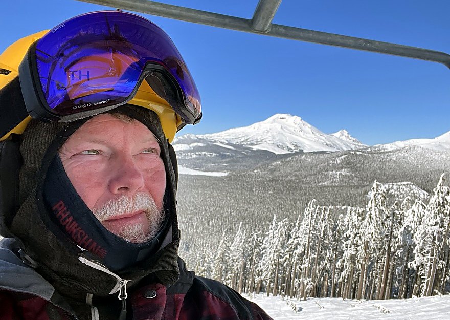 Joel on a chairlift with snowy Cascade peaks behind him.